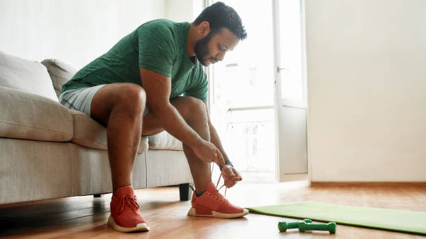 istock Almost ready. Young active man in sneakers tying shoelaces, preparing for morning workout with dumbbells on a yoga mat at home. Fitness, motivation concept 1264557024