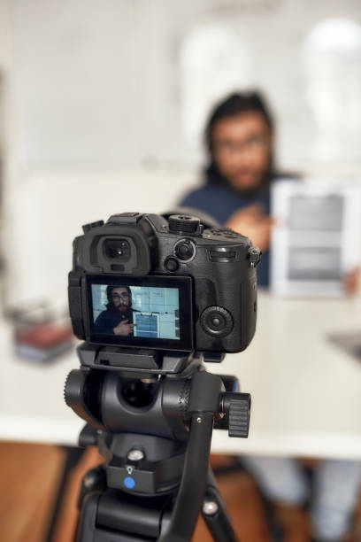 istock Recording video blog. Young man teaching online, explaining new theme while working from home. Focus on camera, professional digital equipment 1264559255