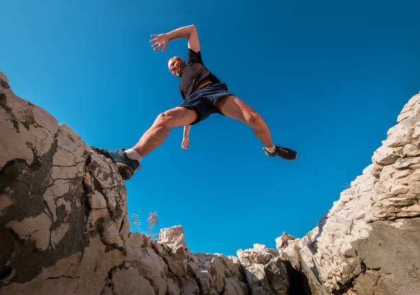 istock Active fast running mountain sky runner smiling and jumping over the cleft cliff during the morning jogging. Sporty people activities a wide-angle concept image. 1264559639