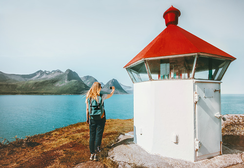 Woman tourist blogging with smartphone taking photo near lighthouse Travel lifestyle adventure summer voyage outdoor in Norway