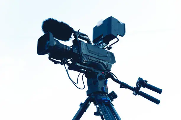 Photo of The video camera with the microphone is standing on the tripod isolated on white, in concept of technology, modern, entertainment.