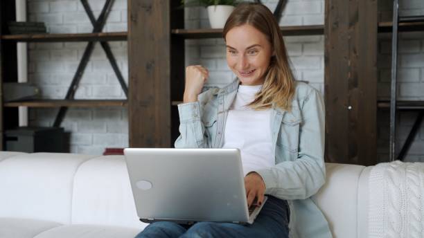 istock Beautiful young woman is using a laptop and smiling while sitting on the sofa at home 1264564575