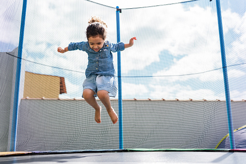 Mixed race boy enjoying camping in summer while jumping on trampoline. He is dressed in retro casual clothing. Exterior of camping site in summer time.