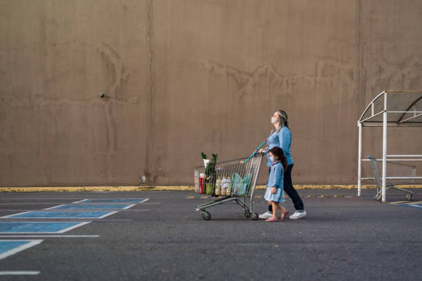 mother and daughter pushing shopping cart in parking lot - pushing women wall people imagens e fotografias de stock