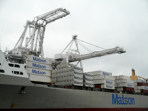 Oakland - July 21, 2010:  Matson Cargo Ship Mahi Mahi loaded with goods at Port by cranes in Oakland Harbor as a tugboat pushes a barge in front of it. The fourth busiest container port in the country, it's a major economic engine in the San Francisco Bay Area.