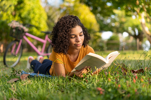 Tenn chica leyendo un libro acostado en la hierba photo