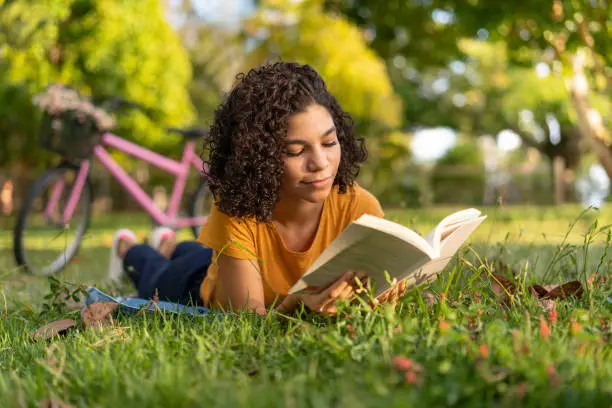 Photo of Tenn girl reading a book lying on the grass