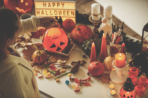 Over the head angle of woman holding a   pumpkin basket above a table decorated with candles, pumpkins and decorative items for Halloween season.