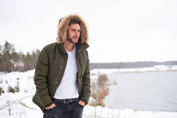 Attractive bearded man standing outdoors in winter season forest. Handsome bearded young caucasian man standing outdoors fur hood in winter season forest. Attractive stylish european guy walking snowy christmas woodland Season holiday leisure winter coat stock pictures, royalty-free photos & images