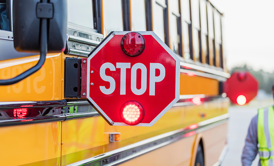 A yellow school bus stopped on the side of the road with stop signs out and flashing.
