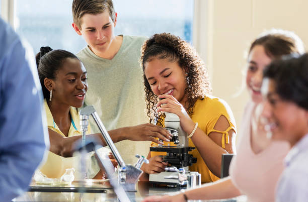 Multi-ethnic high school students in science class A multi-ethnic group of high school students with microscopes in a science lab. The focus is on the teenage boy and two African-American teenage girls working together in the background. high school student classroom education student stock pictures, royalty-free photos & images