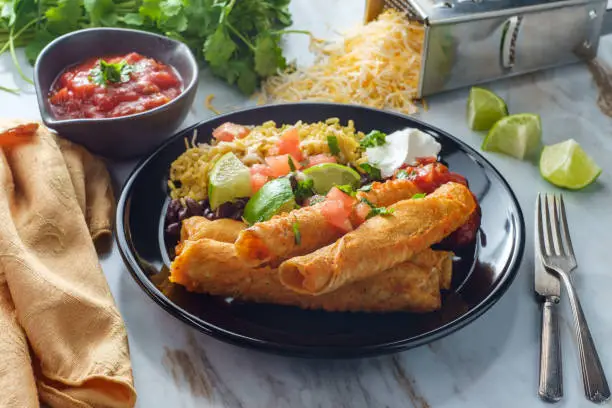 Mexican rolled taco chicken and cheese taquitos with rice and black beans
