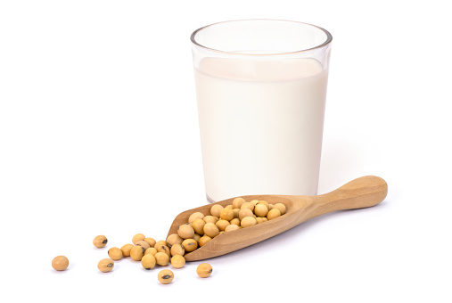 Closeup glass of soy milk and soya beans in wooden scoop isolated on white background. Healthy drinks concept.