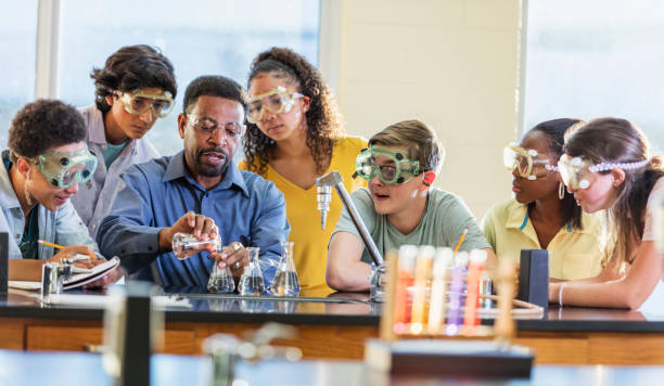 African-American man teaching high school chemistry lab A mature African-American man in his 50s teaching a multi-ethnic group of teenagers in a high school science class. He is performing a chemistry experiment with beakers and test tubes. The students are watching as he pours chemicals from one beaker into another. male meaning stock pictures, royalty-free photos & images