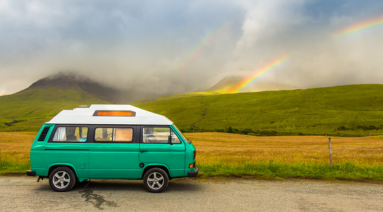 Skye, Scotland - July 5th 2016: An old green camper van in the shadow of the misty Cuillin mountains and a rainbow, at Glen Brittle on the Isle of Skye, Scotland