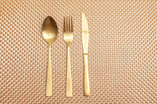 Spoon, fork, knife gold color isolated on gold color background. Top view. Copy space. Horizontal shot.