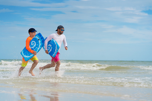 Father and son running with skimboards on shallow waters