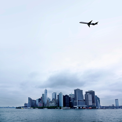 Transportation image of flying silhouetted commercial passenger airplane over cityscape of Manhattan, New York City, USA