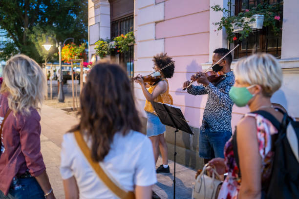 Diverse people with protective face masks watching two afro violin players in the city centre