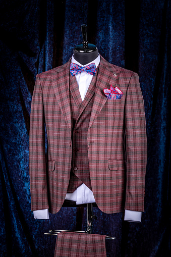 Men's business suit on mannequin, vintage color. elegant three-piece suit in a cage with a bow tie and a scarf in a pocket on blue background