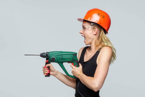 fille blonde. dans un casque de protection orange tient une perceuse dans ses mains. concept de construction - engineer occupation women industrial photos et images de collection