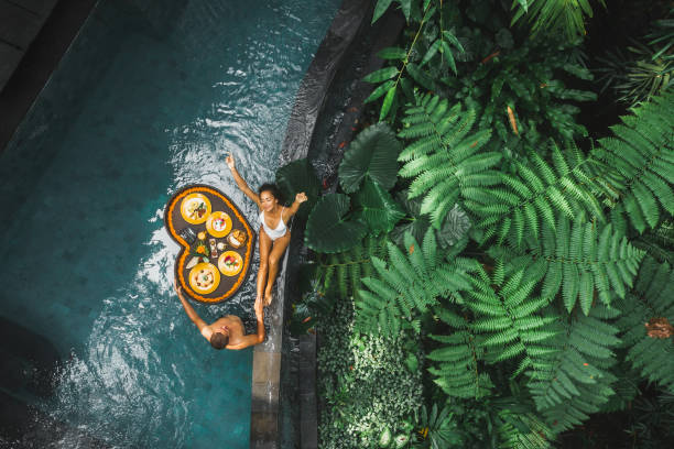 travel happy couple in love eating floating breakfast in jungle swimming pool. awakening in morning. black rattan tray in heart shape, valentines day or honeymoon surprise, view from above. - bali imagens e fotografias de stock