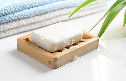White Soap bar with foam on wooden soap dish and cotton towels on white counter table in the bathroom.