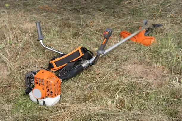 The petrol scythe trimmer brushcutter lies on the hay cut after mowing tall grass in the garden of a country house.