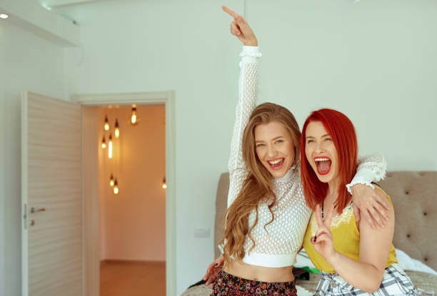 Best friends blonde and redhead indoors having fun shouting and showing signs, laughing and feeling happy
