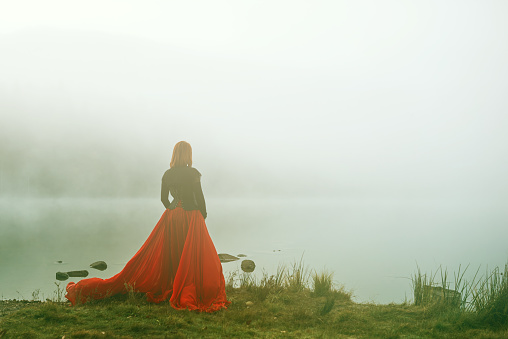 Rear view of woman with red skirt at the lake posing and looking at view