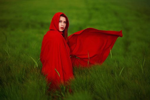 Redhead wearing little red riding hood cap posing outdoors in agricultural field, fairytale concept