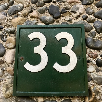 Dark green and white number 33 street address metal plaque placed on stone wall.