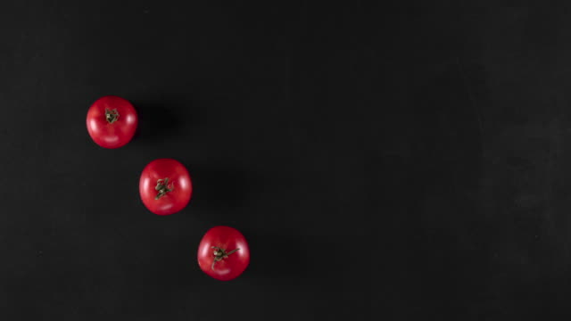 stop motion animation with red tomatoes on a black background, top view, copy space. Concept of vegetarian food or advertisement with vegetables