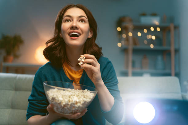 woman watching projector Young woman watching projector, TV, movies with popcorn in the evening. Girl spending time at home. movie theater photos stock pictures, royalty-free photos & images