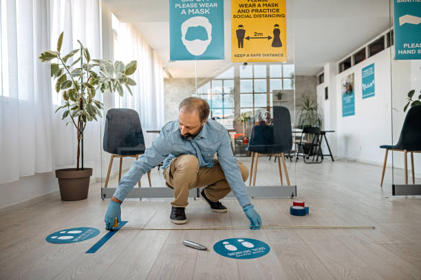 homem aplicando sinal de distanciamento social no escritório - distance measurer - fotografias e filmes do acervo