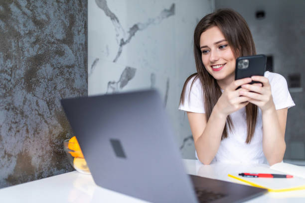 istock Work at home. A young woman use a laptop to work in the kitchen writes something in a notebook with a pen and speaks on the phone 1264645550