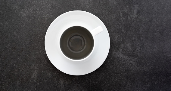 Top down view of empty coffee cup on white saucer placed on dark stone table