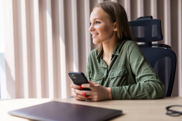 istock Young smiling business woman using smartphone near computer in office 1264651689