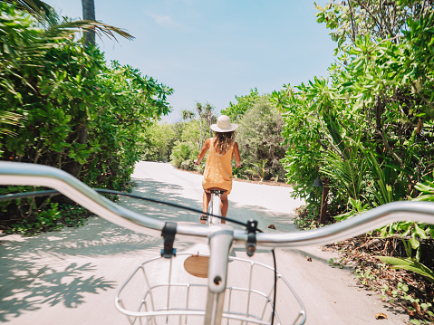 Pov point of view of couple cycling on tropical island. Personal perspective of person cycling with girlfriend in front. Tropical luxury vacations