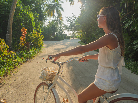 Tropical vacations young woman with bicycle in the Maldives contemplating sunset on the island. Female enjoying bike ride on sandy island. Dreamlike destination