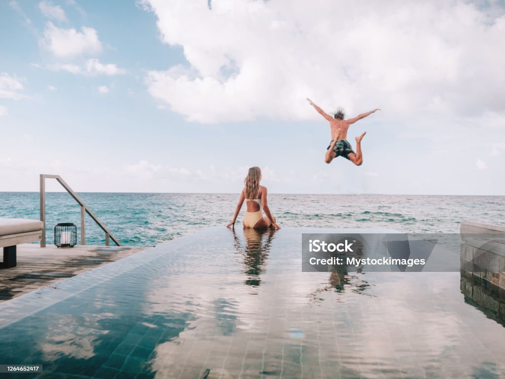 Couple enjoying luxury vacations Couple enjoying tropical vacations from the edge of an infinity pool in private over water villa. People travel luxury holidays Vacations Stock Photo