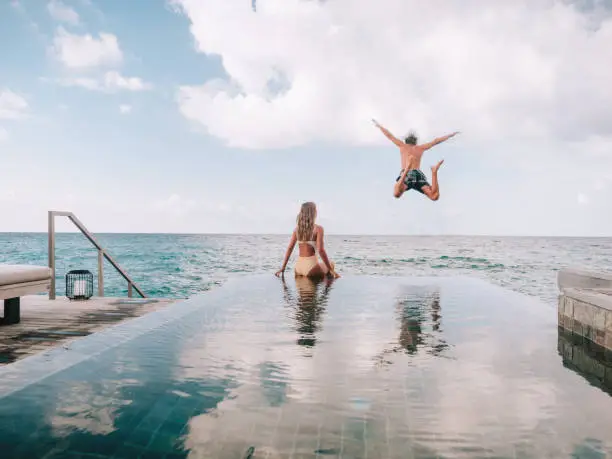 Couple enjoying tropical vacations from the edge of an infinity pool in private over water villa. People travel luxury holidays