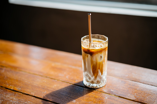 Sot of an iced cold cafe latte next to window on top of wooden table inside a cafe