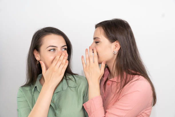 istock Two excited young girls dressed in summer clothes whispering secrets isolated over white background 1264658752
