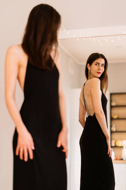 istock Lady wears beautiful black dress looking into the mirror 1264662833