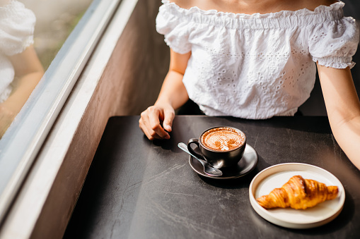 Happy young asian woman having cafe latte and croissant in cafe