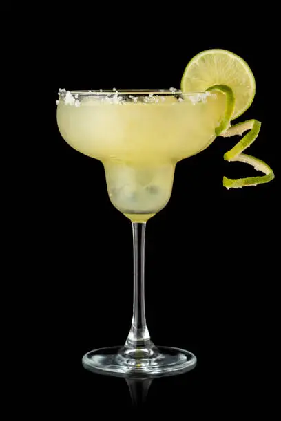 Classic lime margarita cocktail with tequila, triple sec, lime juice, crushed ice and some salt on the rim of a glass, decorated with a slice of lime isolated on white background