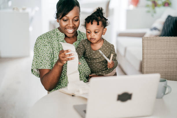 Organizing family finances -mom with baby sitting in front of computer while holding receipt Organizing family finances -mom with baby sitting in front of computer while holding receipt financial wellbeing stock pictures, royalty-free photos & images