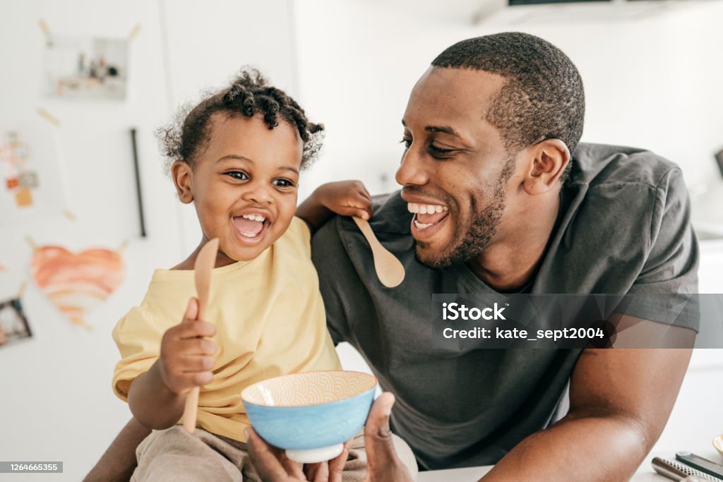 Introducing new meal for your toddler Dad and toddler in the kitchen holding spoons Family Stock Photo