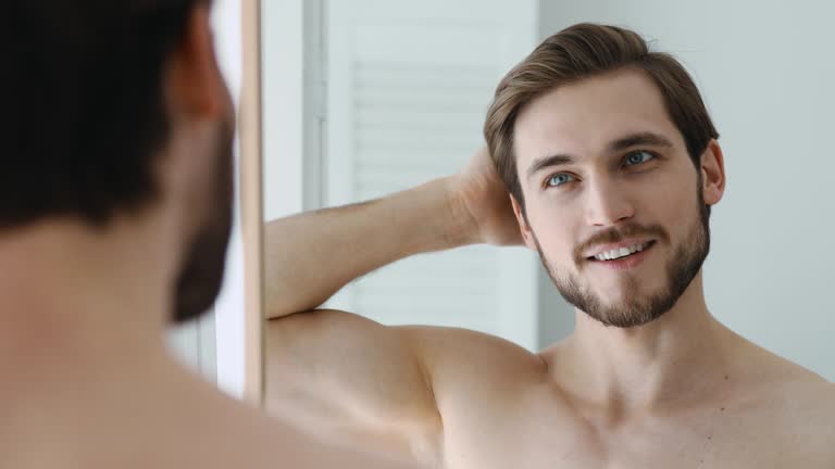 Smiling man combing hair with fingers, getting ready in bathroom.